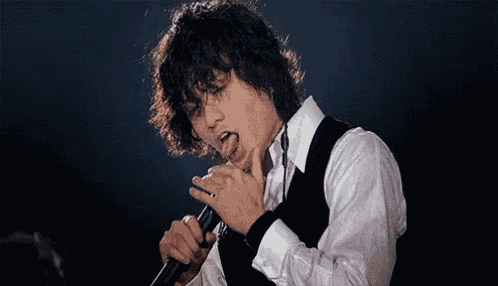 a man with curly hair is singing into a microphone and sticking out his tongue .