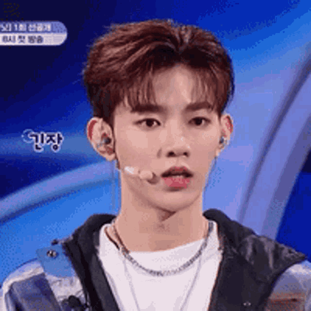 a young man wearing a microphone and a necklace looks at the camera