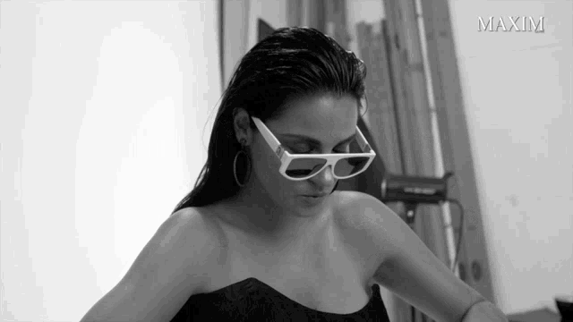 a black and white photo of a woman wearing sunglasses and the word maxim on the bottom right