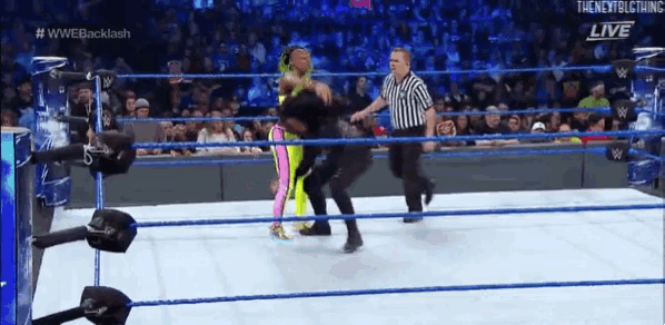 two women are wrestling in a wrestling ring with a referee in the background .