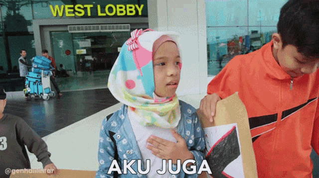 a girl in a hijab stands in front of the west lobby