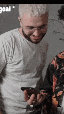 a man in a white shirt is looking at a cell phone with the word goal in the corner