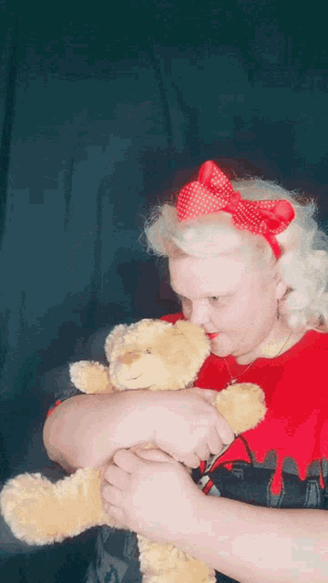 a woman holding a teddy bear with a red bow in her hair