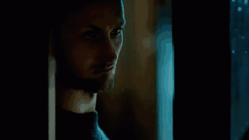 a man with a beard is looking out of a window in a dark room .