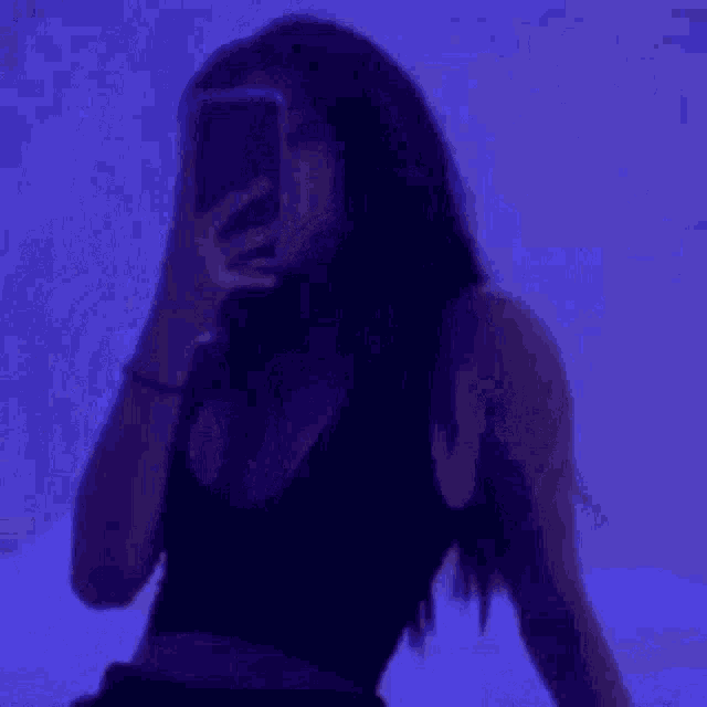 a woman is taking a selfie with her phone in front of a purple background .