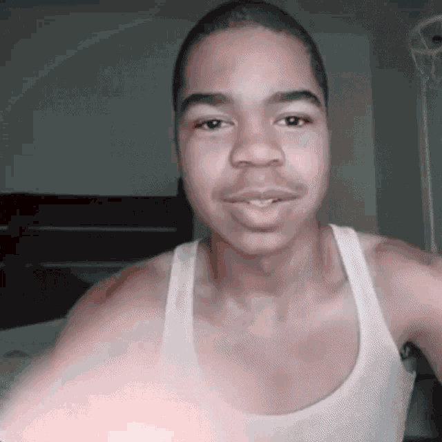 a man wearing a white tank top is smiling for the camera