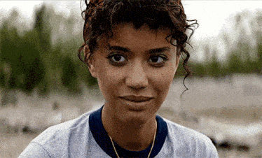 a close up of a woman 's face with curly hair wearing a gray shirt and a blue collar .