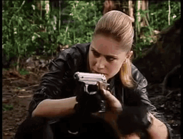 a woman in a leather jacket is holding a gun in her hand .