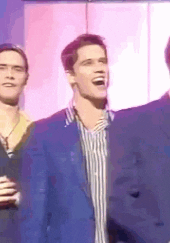 a man in a blue jacket is laughing while standing next to another man in a striped shirt .