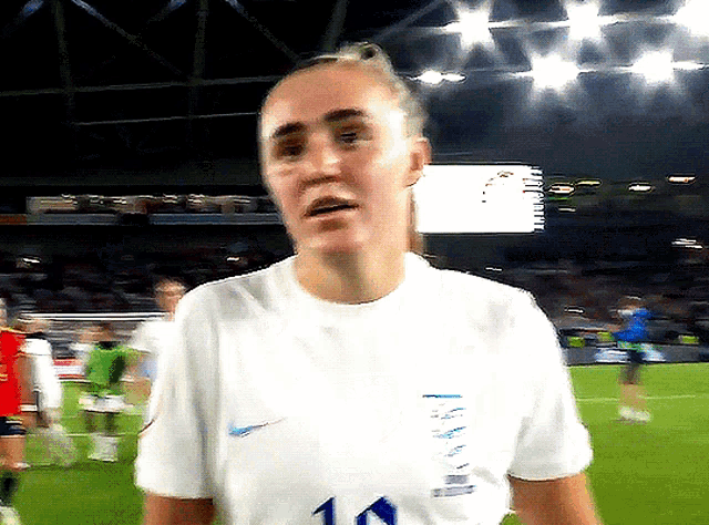 a woman wearing a white shirt with the number 10 on it stands on a soccer field