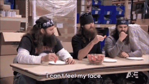 three bearded men are sitting at a table eating food and one of them is saying i can 't feel my face