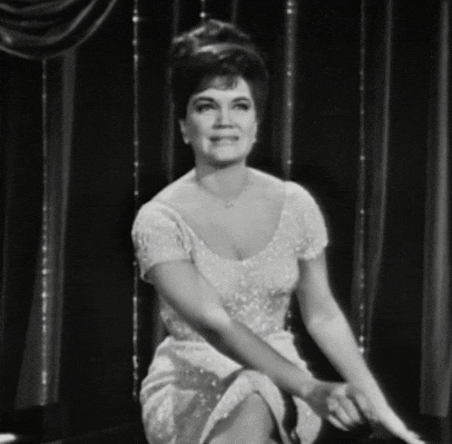 a woman in a white dress is sitting in front of a curtain