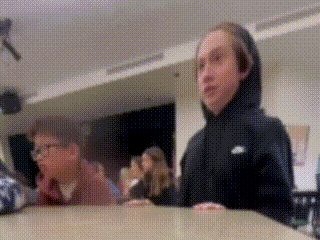 a blurry picture of two people sitting at a table in a room . one of the people is wearing a nike hoodie .