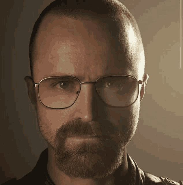 a man with glasses and a beard looks at the camera with a serious look on his face