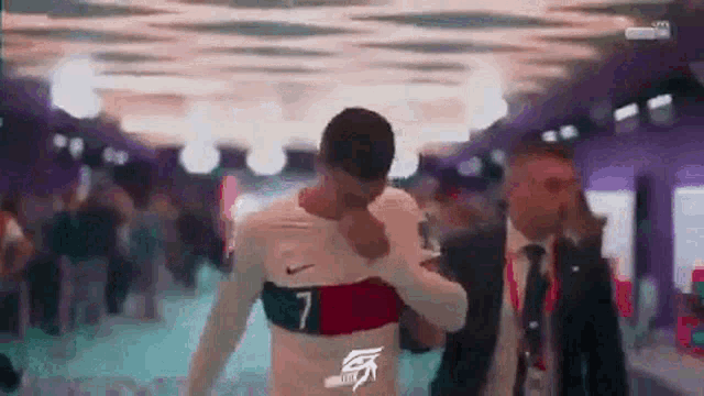 a man in a suit and tie is standing next to a man in a soccer jersey .