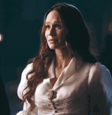 a woman with long hair is wearing a white shirt and a brooch on her chest .