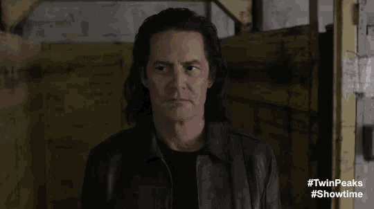 a man in a black leather jacket says " kindergarten " in front of a yellow wall