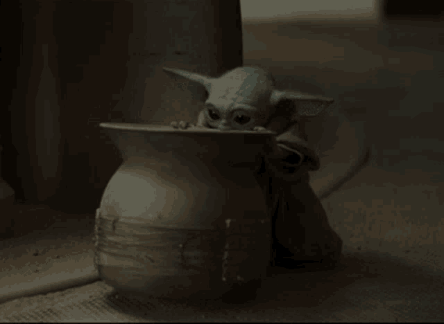 a baby yoda figurine sits next to a large vase
