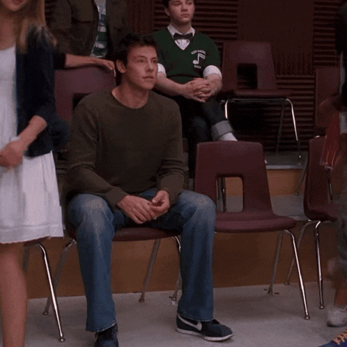 a man sitting in a chair wearing a green sweater that says ' abercrombie & fitch ' on it