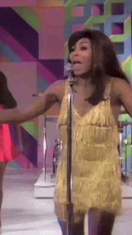 a woman singing into a microphone with her arms outstretched