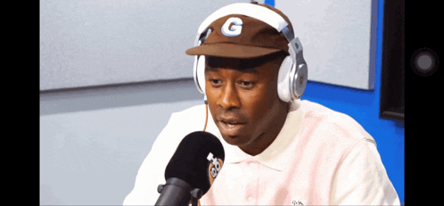 a man wearing headphones and a hat with the letter g on it talks into a microphone