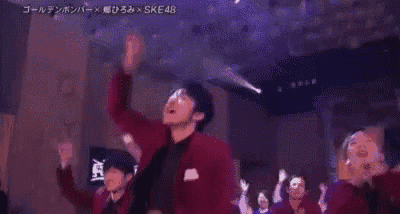 a man in a red jacket is dancing in front of a crowd with a sign that says ske48