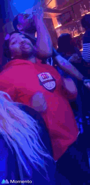 a woman in a red shirt is dancing in a crowd with the word momento on the bottom right
