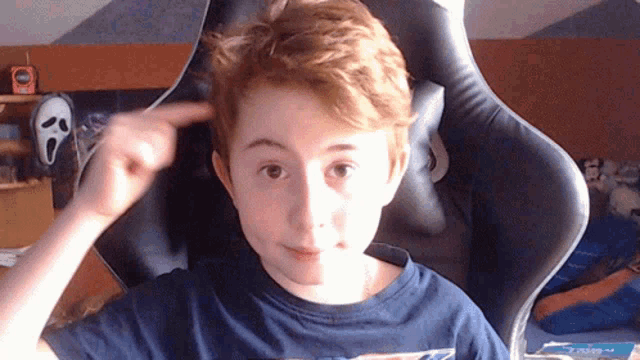 a young boy is sitting in a chair with a scream mask on the wall behind him