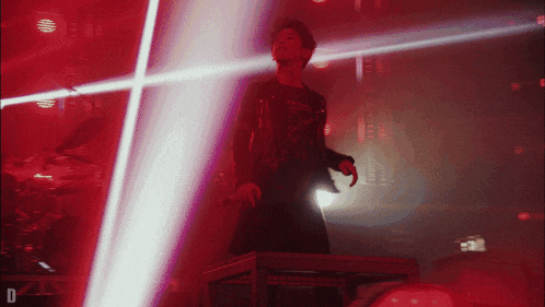 a man stands on a stage in front of a red light with the letter d on the bottom right