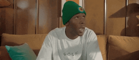 a man is sitting on a couch wearing a green beanie and a white shirt .