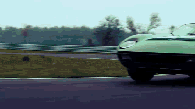 a green car is driving on a road with a fence in the background