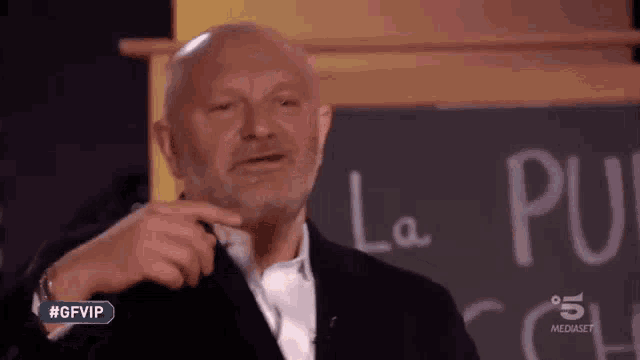 a bald man with a beard is standing in front of a blackboard with the word la written on it