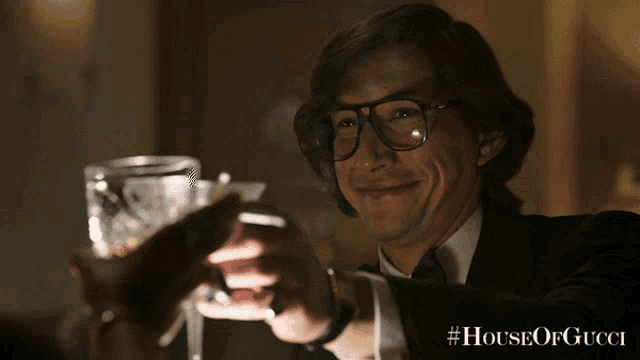 a man wearing glasses and a tuxedo is toasting with two glasses of wine