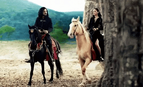 a man and a woman are riding horses on a dirt road .