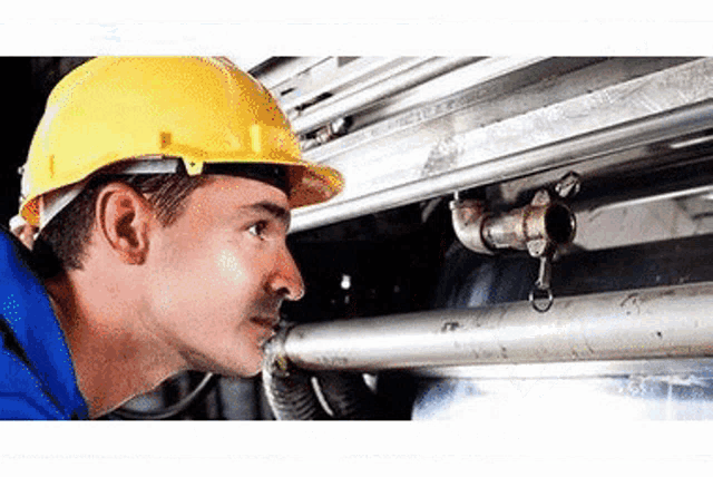 a man wearing a yellow hard hat is looking at a pipe .