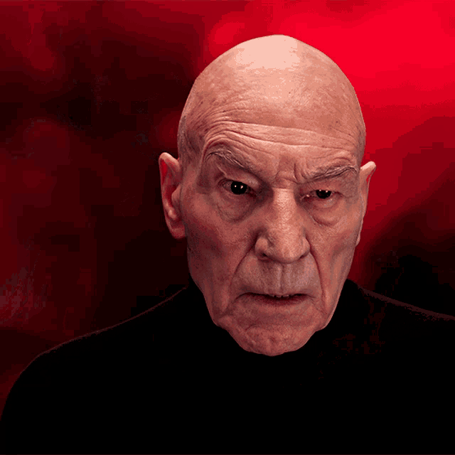 a bald man with a black shirt is looking at the camera with a red background