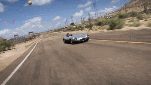 a car is driving down a road with a hot air balloon in the sky