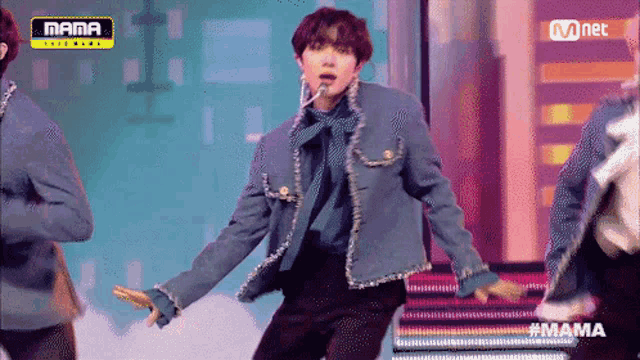 a man in a blue jacket stands on a stage in front of a mnet sign