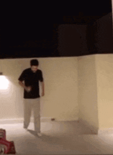 a man in a black shirt and white pants is standing in front of a wall at night .