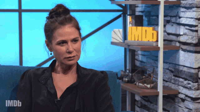 a woman sits on a couch in front of a shelf that says imdb