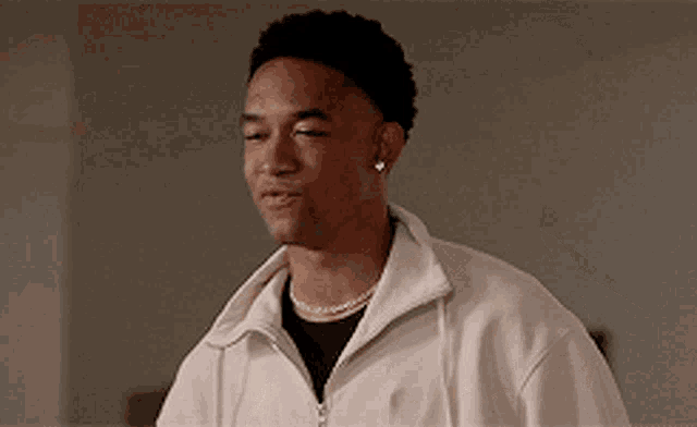 a young man wearing a white jacket and a black shirt is looking at something .
