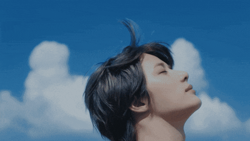 a woman looks up at the blue sky with clouds
