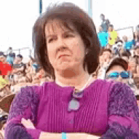 a woman in a purple sweater is standing with her arms crossed in front of a crowd of people .