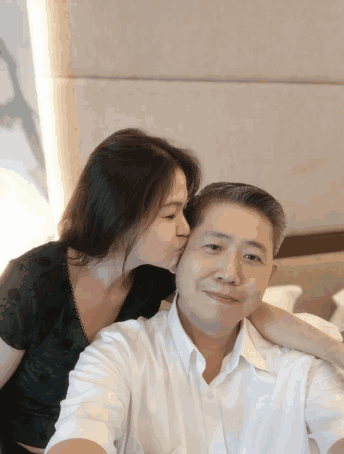 a woman kisses a man on the cheek while taking a selfie