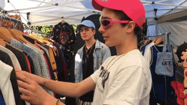 a man wearing a pink hat and sunglasses looks at a guess shirt