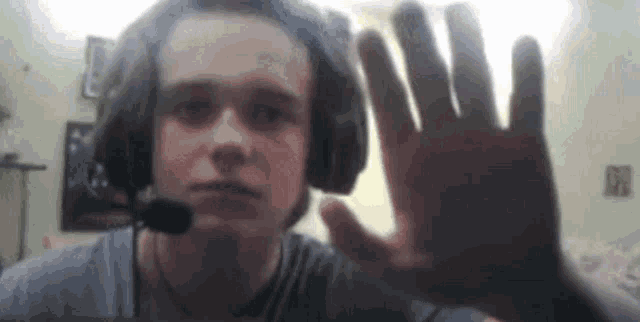 a young man wearing headphones and a microphone is waving his hand in front of a camera .