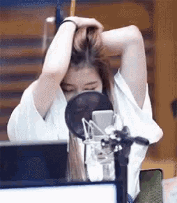 a woman is standing in front of a microphone holding her hair .