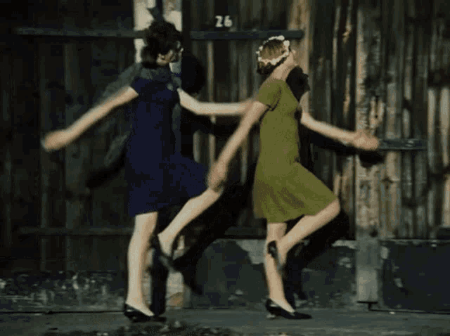 two women are dancing in front of a building with the number 26