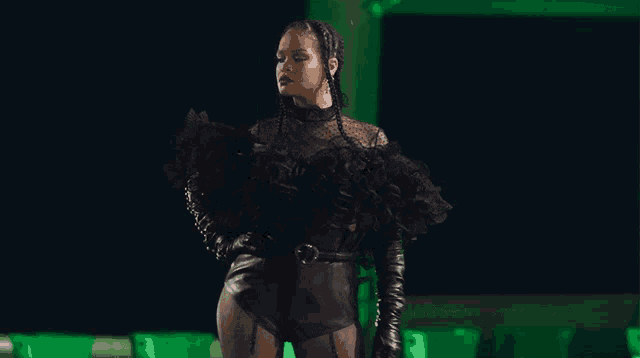 a woman in a black bodysuit and leather gloves stands in front of a green background