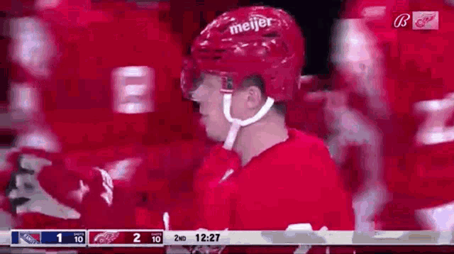 a hockey player wearing a red helmet is standing in front of a scoreboard .